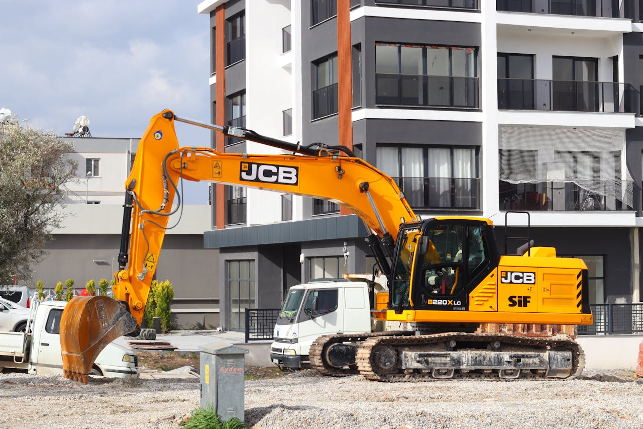 home-services-01 A yellow excavator operating at a city construction site in front of modern buildings.